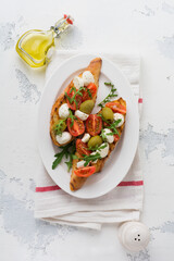 Caprese bruschetta toasts with mozzarella, cherry tomatoes, olives and arugula. Top view with space for your text.
