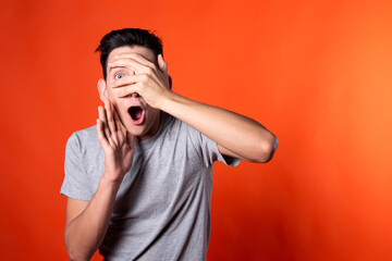The young guy overhears and is surprised. Orange background. Blue jacket. Emotions and feelings.