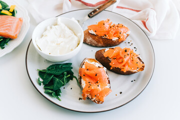 Delicious toast with salmon and cheese cream on a white plate whit spinach.