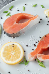 Juicy fresh salmon steak in a white plate on a wooden cutting board with onion, lemon and spices on a natural slate stone table, close-up. Deliciously cooked salmon fillet...