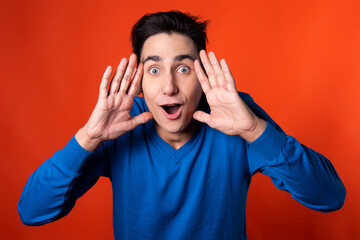 The young guy overhears and is surprised. Orange background. Blue jacket. Emotions and feelings.