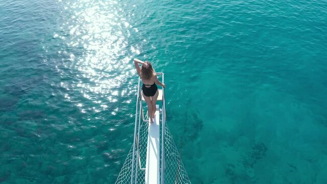 Happy girl stand on bow of sailing boat have fun discovering islands in tropical sea on summer coastal cruise. Aerial view 4K.