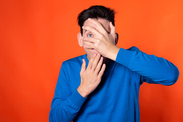 The young guy overhears and is surprised. Orange background. Blue jacket. Emotions and feelings.