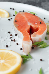 Juicy fresh salmon steak in a white plate on a wooden cutting board with onion, lemon and spices on a natural slate stone table, close-up. Deliciously cooked salmon fillet...