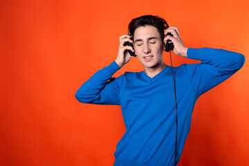 Handsome guy listens to music with headphones. Technology and gadgets. Orange background.