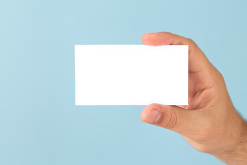 Fototapeta premium Male hand holding blank business card on light blue background