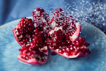 Delicious cut pomegranate fruit under drops of water on a blue dish.