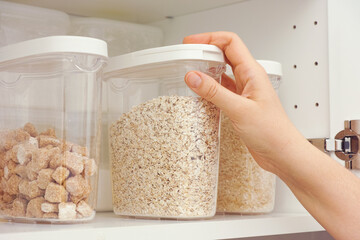 Woman taking oat flakes from a kitchen cupboard. Close up.