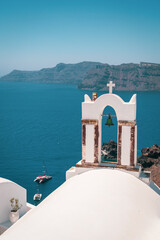 Arch with a bell, white houses and church with blue domes in Oia village. Island Santorini, Greece