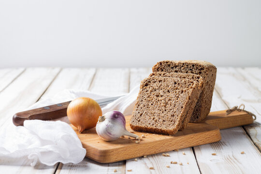 Sliced slices of spelt bread with onion and garlic lie on the kitchen board on a light wooden background.