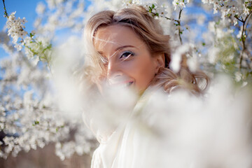 Portrait of pretty blong girl posing against the spring flowers. Woman enjoy the healthy aroma smelling in the garden