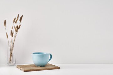 Croissant and a mug on a wooden stand, a vase and a pot with a plant on the books, white background. Eco-friendly materials in interior decor, minimalism. Copy space, mock up.