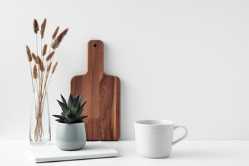 A mug, a potted houseplant, a clear vase and a wooden cutting board. Eco-friendly materials in the decor of the room, minimalism. Copy space, mock up