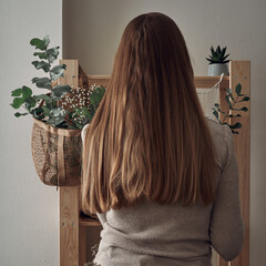 The girl decorates a wooden rack with an eco-bag with eucalyptus branches, flowers, houseplants. Eco-materials, storage. Folk.