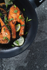 Juicy grilled salmon steak with lemon, spices and lime in a pan on a natural slate stone table, close-up. Deliciously cooked salmon fillet