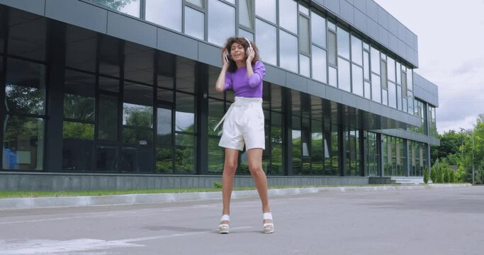 full length of woman listening music in headphones and dancing outside