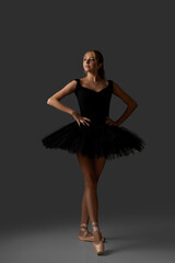 Naklejka premium Young ballerina in black tutu and pointe shoes is dancing on studio background