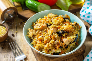 Bulgur with turkey and prunes is served with fresh vegetable on a rustic table.