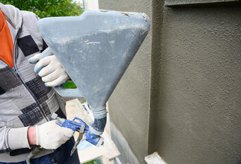 A building contractor is renovating, rendering exterior walls of the house, applying stucco,...