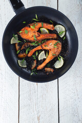 Juicy grilled salmon steak with lemon, spices and lime in a skillet on a light wooden table. Deliciously cooked salmon fillet