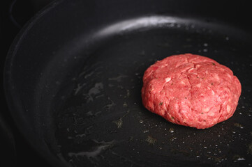 Hamburguesa de carne cruda en sartén negra con aceite