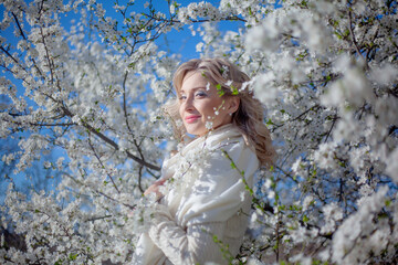 Portrait of pretty blong girl posing against the spring flowers. Woman enjoy the healthy aroma smelling in the garden