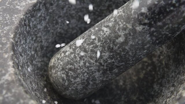 Fresh sea salt is falling into the grey stone mortar in slow motion