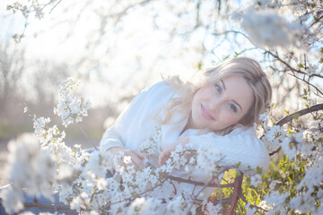 Portrait of pretty blong girl posing against the spring flowers. Woman enjoy the healthy aroma smelling in the garden