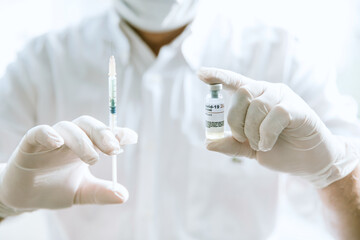 Doctor in protective gloves & medical mask holding injection syringe and COVID-19 vaccine