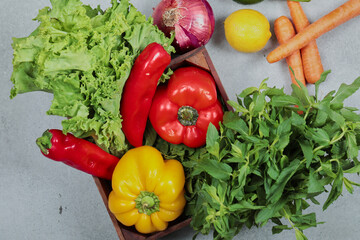 Wooden box of fresh peppers, carrots, lime, lemon, mint and lettuce on gray background