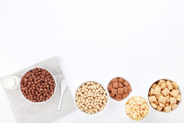 Various corn flakes with bottle of milk and spoon on white wooden table