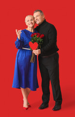 Mature couple with heart and flowers on color background. Valentine's Day celebration