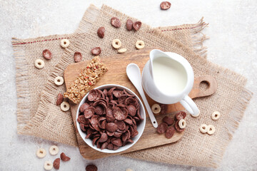 Chocolate corn flakes with milk in jar and granola bar on grey background