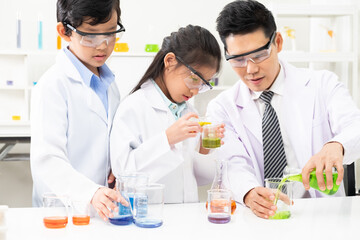 Young Asian kids wearing white scientist gown and do chemical test tube while study, learning in science classroom with teacher. Young children education concept by experiment, fun and enjoy classroom