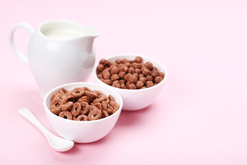 Chocolate corn flakes with milk in jar and spoon on pink background
