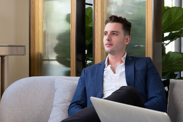 Adult Caucasian businessman dress in smart formal suit sitting inside modern office space drinking coffee while waiting and planning for business meeting. Entrepreneur concept with copy space.