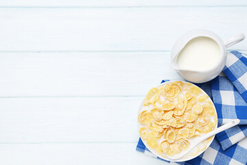 Corn flakes in bowl with milk and blue napkin on wooden table