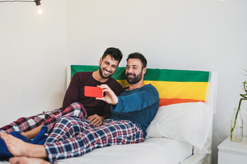 Gay men couple taking a selfie with smartphone in the morning while wearing pajama inside bedroom at home