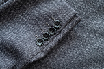 High resolution with details and quality shot of formal black or dark grey wool suit fabric texture. with button decoration under light and shadow ambient. Ideal for background or wallpaper.