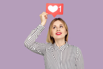 Cute happy woman with red lips in glamour striped blouse holding social media heart Like icon over head