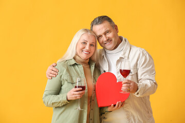 Mature couple with gift box and wine on color background. Valentine's Day celebration