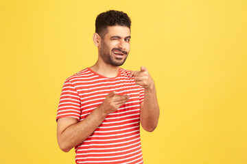 Excited mischievous man with beard in striped t-shirt winking looking and pointing fingers at...