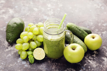 Green smoothie in glass jar with fruits and vegetables on black background