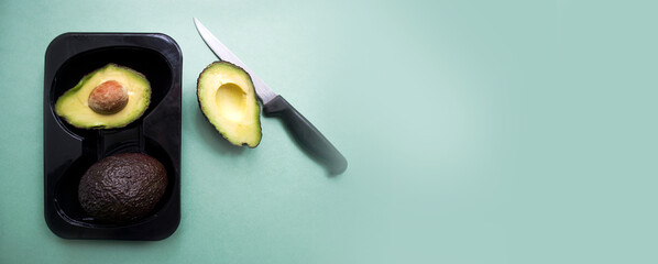Hass varieties avocado top view, ripe avocados in dark black plastic packaging on a green background. Whole and halved avocado.Banner. Copy space.