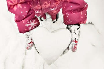 Children's hands in warm mittens with a snow-white heart made of snow. The Concept Of Valentine's Day
