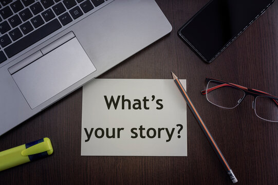 What's your story card. Top view of office table desktop background with laptop, phone, glasses and pencil with card with inscription what's your story.  Business concept.