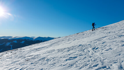 A man wearing snow shoes hiking up along a steep slope to the peak of Speikkogel in Austrian Alps. The whole slope is covered with snow. many mountain chains in the back. Winter outdoor activity.