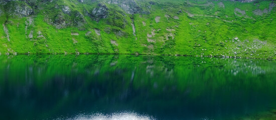 wonderful reflection from green hills in a mountain lake panorama