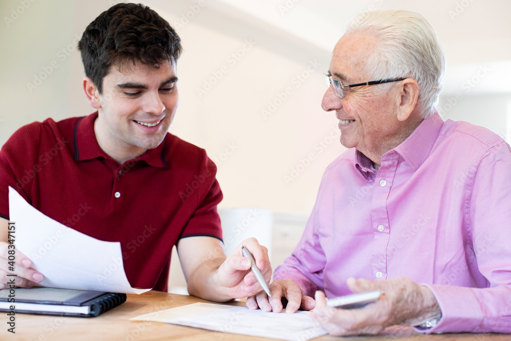 Wall mural Young Man Helping Senior Neighbor With Paperwork At Home