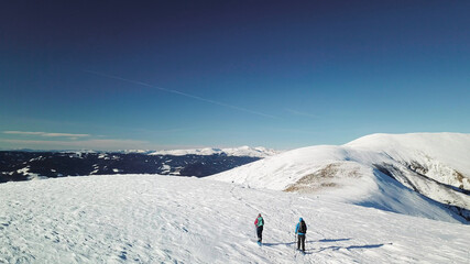 A drone shot of a couple wearing snow shoes hiking up to the peak of Speikkogel in Austrian Alps. The whole slope is covered with snow. many mountain chains in the back. Winter outdoor activity. Fun